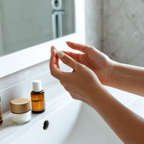 **

A close-up shot of a woman with sensitive skin carefully applying a solid perfume to her wrists. She's in a well-lit, minimalist bathroom with natural light. The focus is on her gentle touch and the natural ingredients of the perfume.  Fully clothed, appropriate content, safe for work, perfect anatomy, natural proportions, professional. Emphasis on the Italian concept of "cura di s&eacute;" (self-care).

**